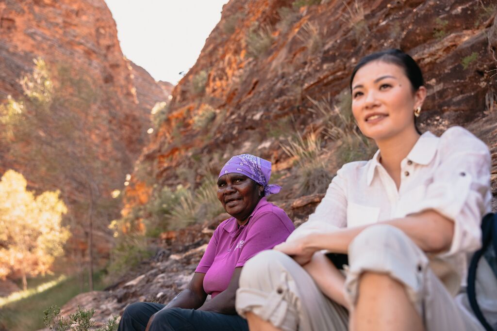 A woman sitting beside a Western Australian First Nations woman against the backdrop of the striking rock formations of the Bungle Bungle Range in Purnululu National Park, Kimberley.